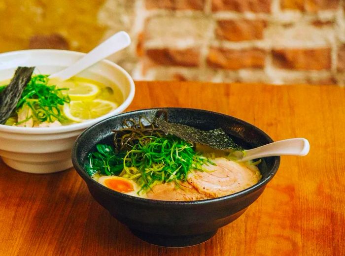 Two bowls of ramen resting on a wooden counter.