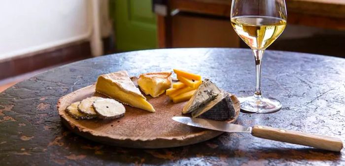 A platter showcasing various cheeses, accompanied by a knife and a glass of wine nearby.