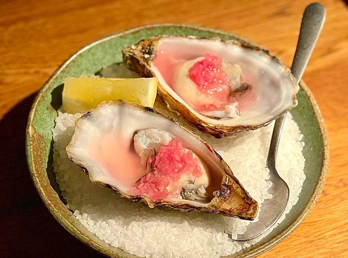 Two oysters, lightly tinted pink, served with mignonette atop a bed of ice.