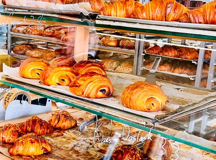 A display case showcasing trays of croissants and pastries, with prices elegantly written on the glass.