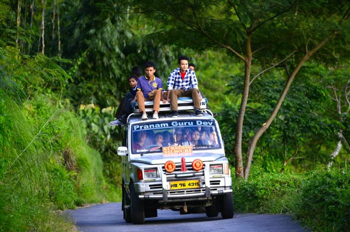 A shared taxi filled with passengers navigates a narrow mountain road.