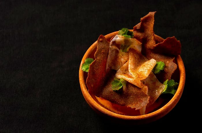 A bowl filled with layers of chips and various ingredients set against a dark background.