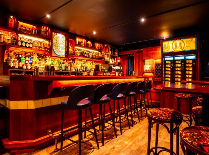 The bar features illuminated shelves filled with bottles, cozy stools around a round wooden bar, and a colorful vending machine.