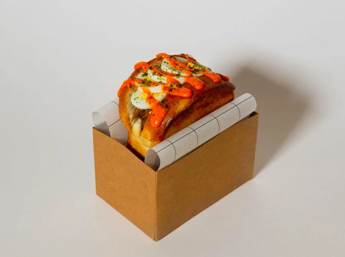 A sandwich peeking out from a cardboard box, adorned with a variety of sauces.