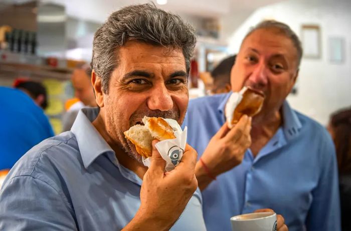 Two customers indulge in large, cream-filled buns.