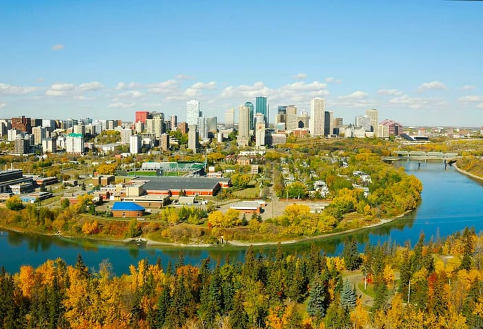 A city featuring several skyscrapers alongside a river, enveloped by lush greenery.