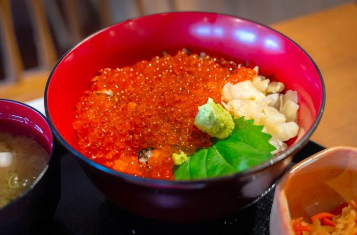 A bowl brimming with bright orange roe and various toppings over a bed of rice.