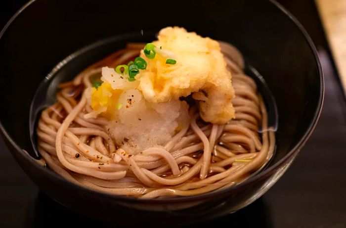 A bowl of soba noodles in savory broth, topped with crispy tempura.