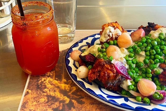 A serving of Chicken Fried Chicken (fried chicken topped with chorizo verde gravy, pearl onions, and peas) accompanied by a mason jar Bloody Mary from Dove’s Luncheonette in Chicago