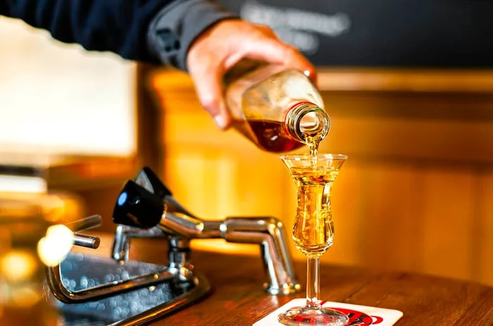 A bartender in Amsterdam serves jenever/genever into a tulip-shaped shot glass as part of the kopstootje tradition.