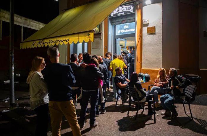 A crowd gathers at night outside a bakery.