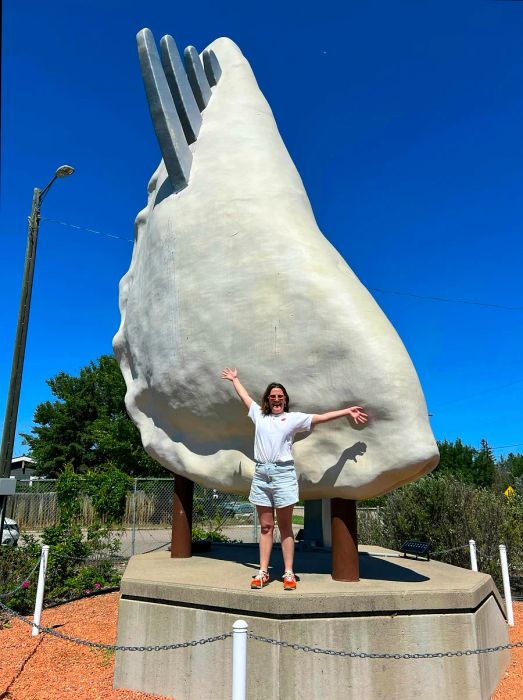 A woman stands in front of a towering sculpture of a dumpling with a fork piercing it, showcasing its impressive size.