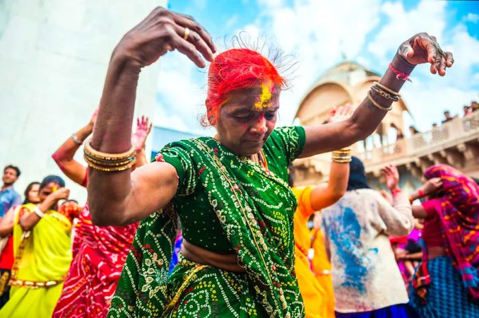 A close-up of a woman in vibrant attire dancing amidst a crowd during the Holi festival.