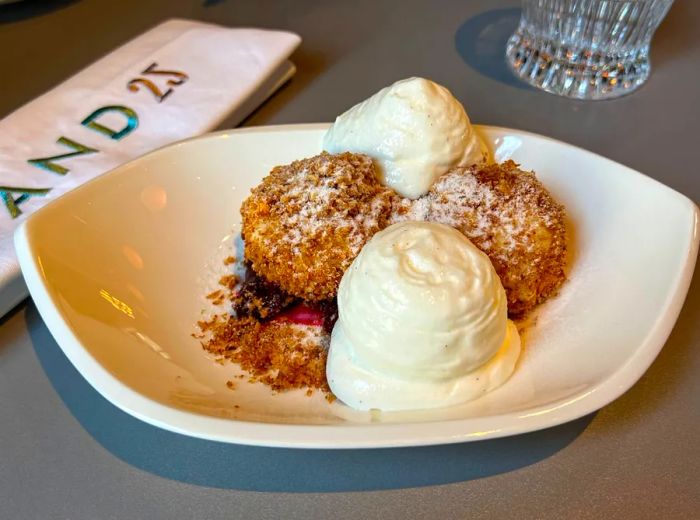 Two breaded dumplings accompanied by two scoops of sour cream, with cherries peeking out from beneath.