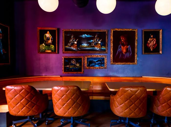 Two bar tables joined by a wooden banquet, accompanied by leather swivel chairs, set against a backdrop of playful art.