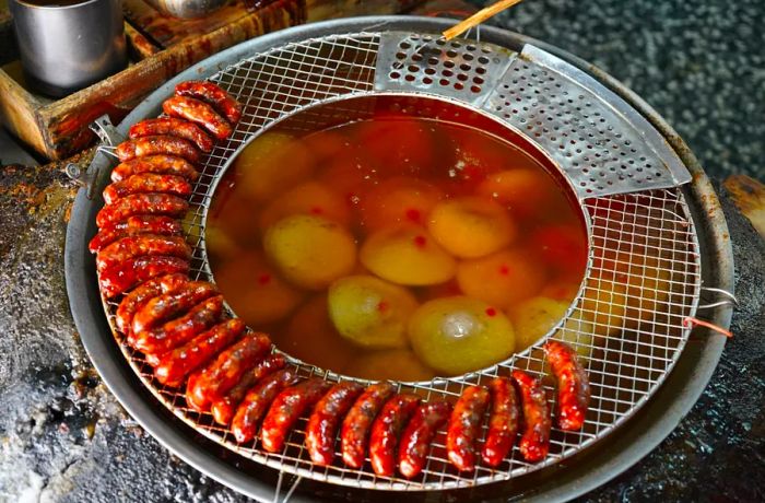 Meatballs soaking in a vat, with sausages neatly arranged on a rack around the edges of the pot.