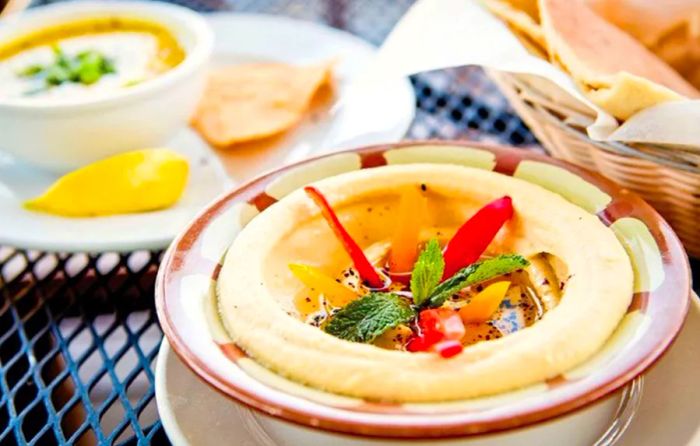 A bowl of hummus garnished with crudités on a metal outdoor table.