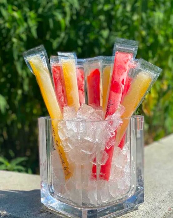 A pitcher filled with ice and colorful, plastic-wrapped popsicles protruding from it.