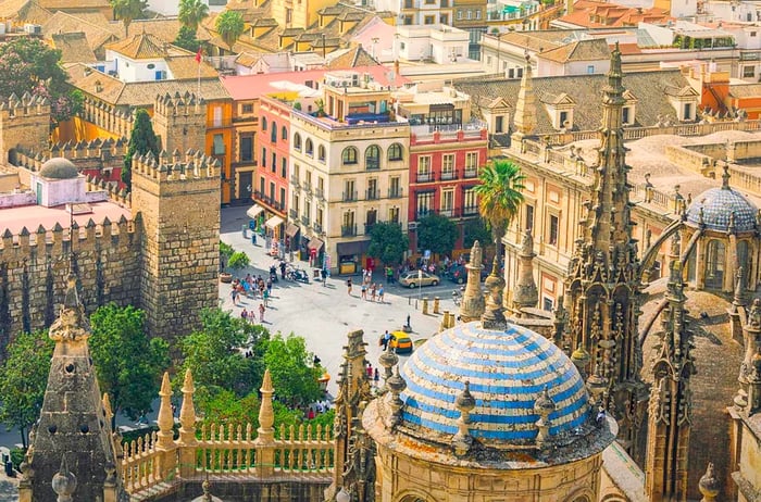 A grand cathedral with a dome and turrets overlooking a bustling city square below.