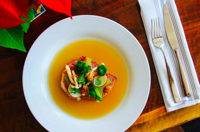 An overhead view of a soup bowl featuring a thick slice of ham adorned with various toppings in a rich sauce.