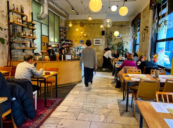 A spacious cafe with high ceilings where diners enjoy their meals at tables, illuminated by globe pendant lights, while a server navigates the central aisle.