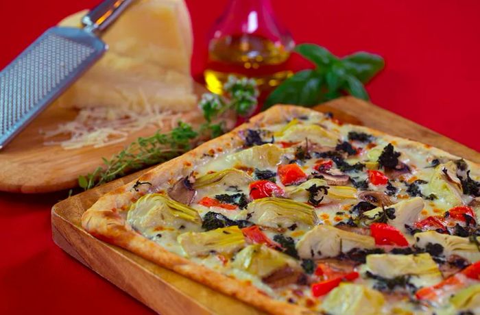 A square pizza placed on a wooden block alongside a block of shaved cheese.