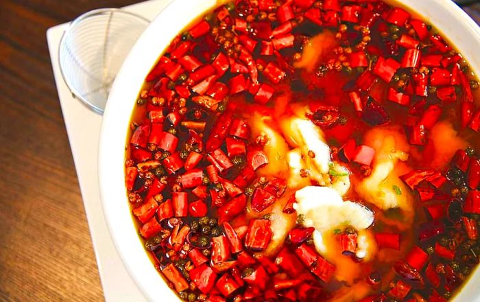 A bowl of stew brimming with peppercorns and chunks of whitefish.