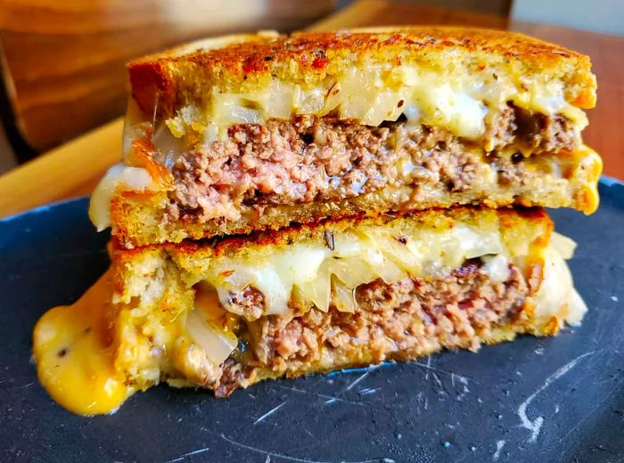 A burger sliced in half, with cheese oozing onto a marble plate.