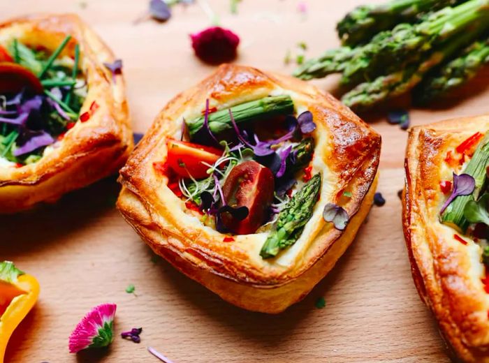 A square puff pastry tart adorned with asparagus, tomatoes, and greens.