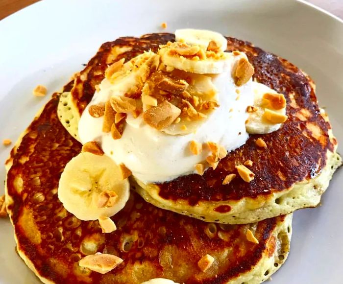 A plate featuring two thick pancakes layered with banana slices and brittle.