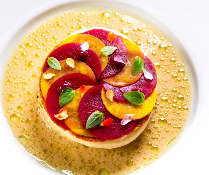 Celery and beet slices elegantly arranged on a circular plate, surrounded by a broth.