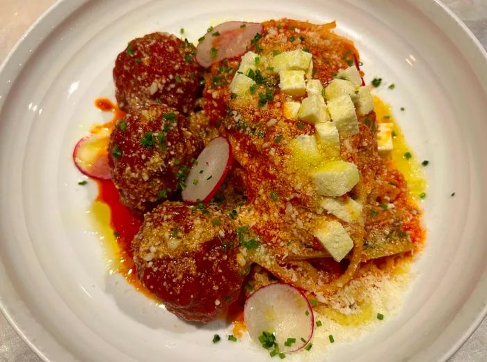 A dish of pasta accompanied by sauces and chunks of cheese, alongside three hearty meatballs.