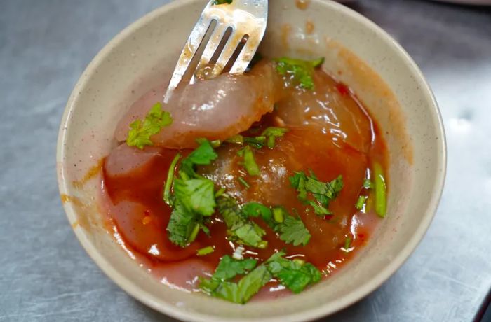 A fork lifts a morsel of meat from a bowl filled with jelly-like meatballs.