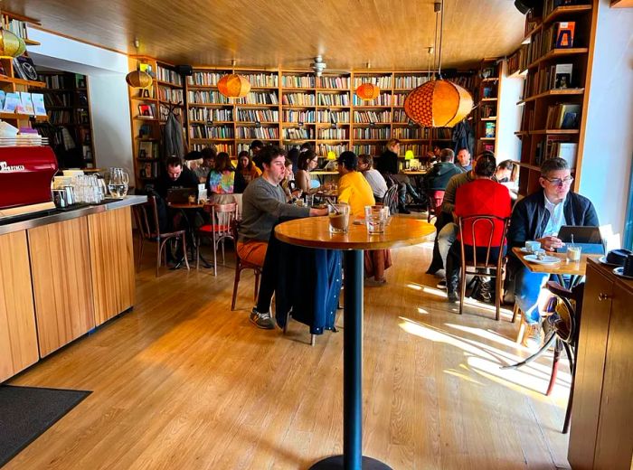 Patrons enjoying their time at tables in a sunlit café, with expansive bookshelves in the background.