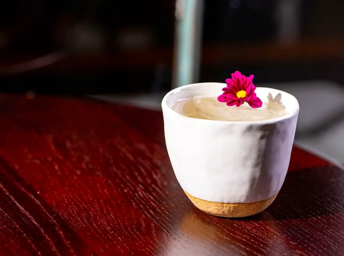 A cocktail served in a clay cup, adorned with a purple flower on top.