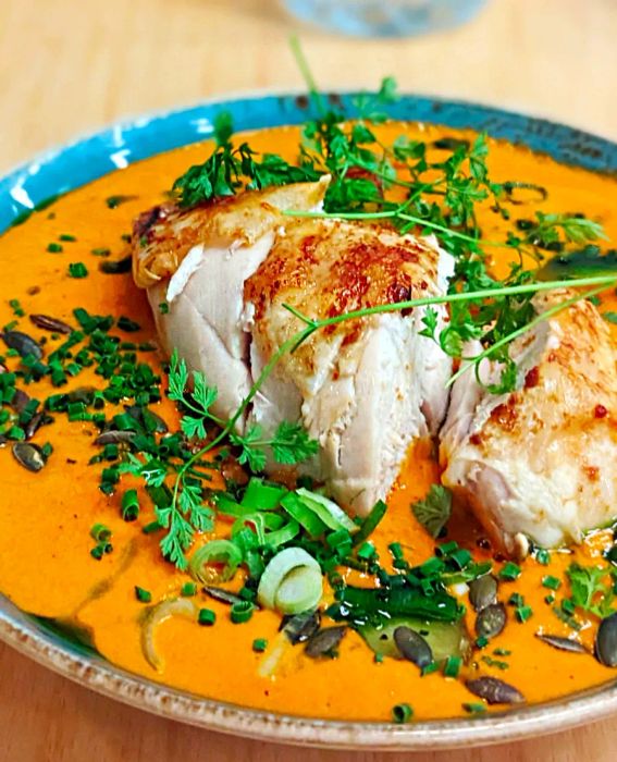 Tender slices of chicken bathed in a vibrant orange sauce, garnished with chopped herbs.