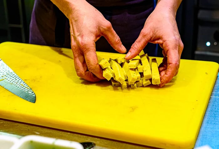 A chef collects raw panisse sticks on a cutting board.