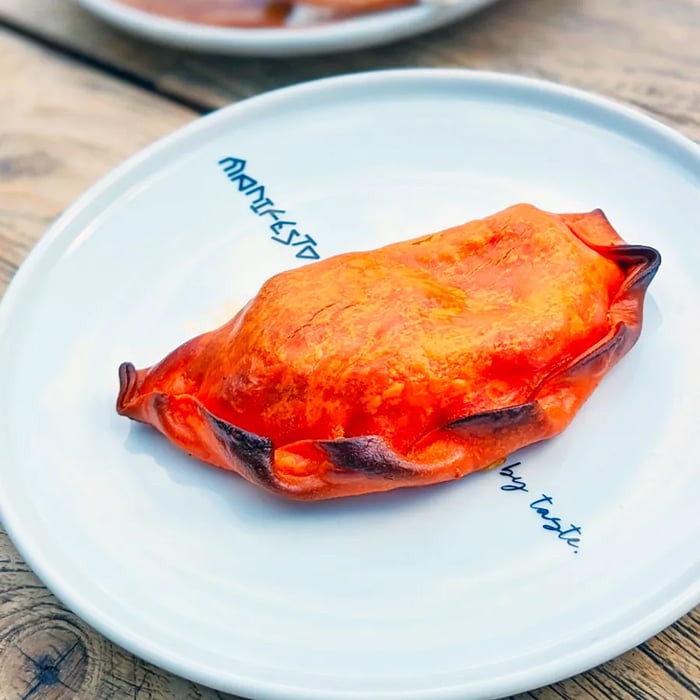 An empanada displayed on a pristine white plate atop a wooden picnic table.