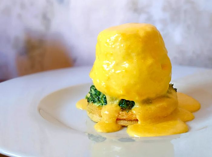 A towering eggs Benedict generously drizzled with sauce.