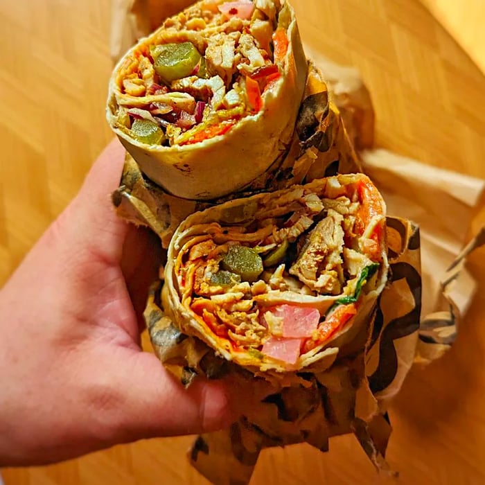 A hand presents a shawarma wrap sliced in half, showcasing its delicious fillings.