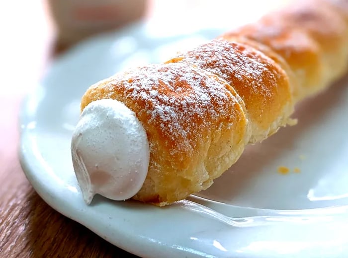 A pastry rolled and overflowing with creamy filling, dusted with powdered sugar.