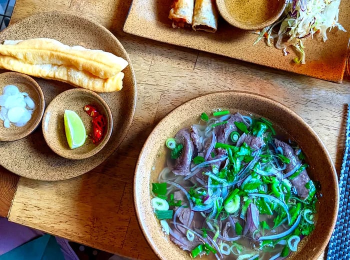 A bowl of pho garnished with toppings and accompanied by spring rolls.