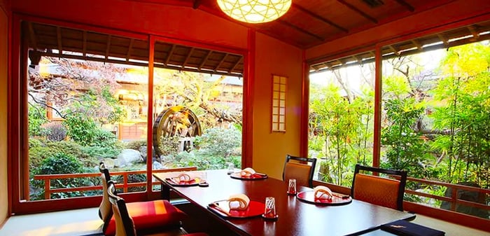 A dining table arranged in a spacious room with large windows that overlook a sunny garden.