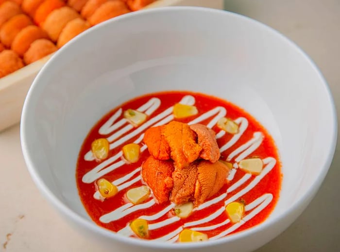 Uni slices nestled in a vibrant red broth, elegantly finished with a drizzle of white sauce.