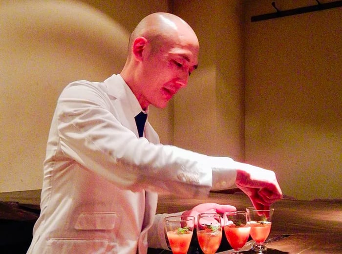 A bartender meticulously garnishes a lineup of cocktails on a dark wooden bar.