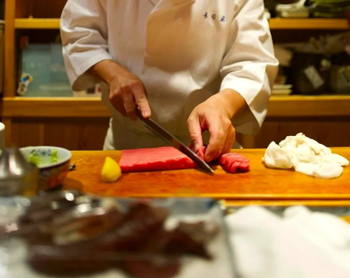 A chef skillfully slices a long piece of fish at the sushi counter.