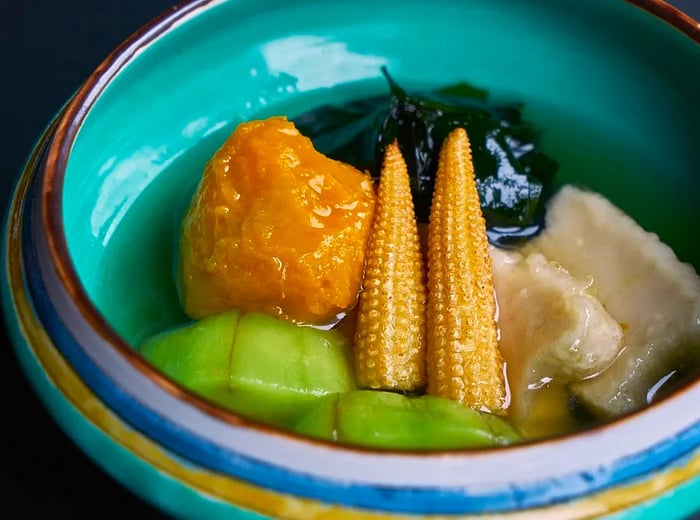 A vibrant blue ceramic bowl filled with a variety of cooked vegetables in broth.