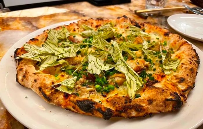 A complete white pizza adorned with bonito flakes and konbu.