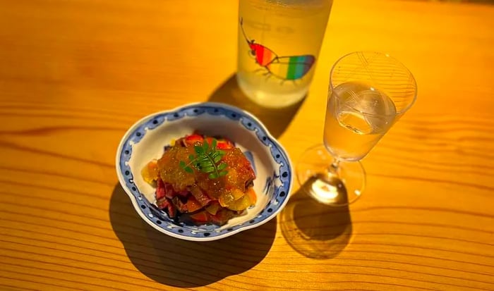 A petite snack elegantly presented in a decorative dish, accompanied by an ornate sake glass and a bottle.