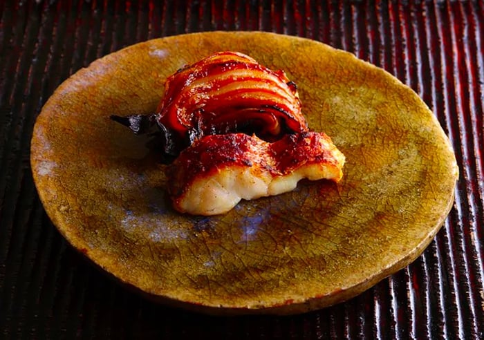 A beautifully roasted fish presented on a dark gold plate.